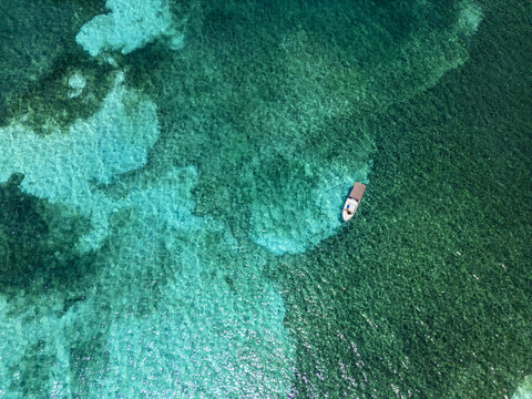 Aerial view of a small boat floating on crystal clear turquoise waters over a coral reef Guanaja, Bay Islands Department, Honduras.