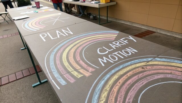 Colorful Chalk Art on a Table Featuring Words Plan, Clarify, and Motion at an Outdoor Event in a Community Setting