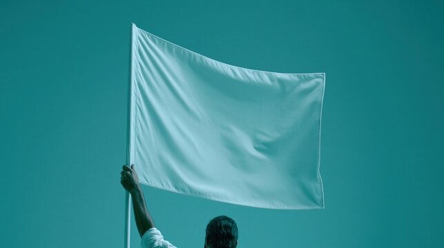 Back view of person holding up plain solid white waving flag against solid teal background representing freedom new start and independent movement