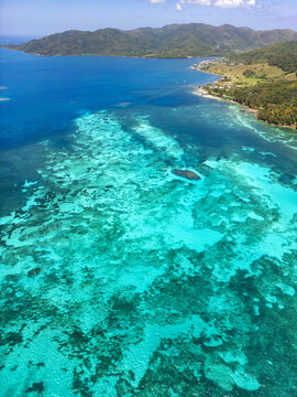 Aerial view of the vibrant turquoise coral reefs and lush green hills along the tropical coastline Guanaja, Bay Islands Department, Honduras.