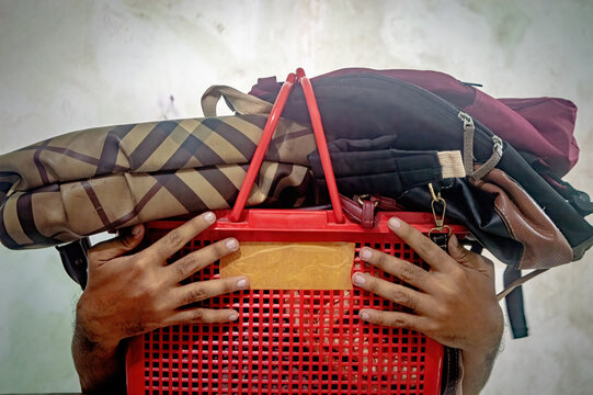 Close up of a man holding a red plastic basket filled with various bags, showcasing the concept of carrying a heavy load and the challenges of balancing multiple responsibilities