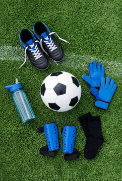 Soccer equipment including a ball, cleats, shin guards, gloves, socks, and water bottle laid on artificial turf