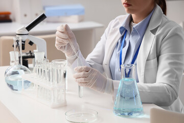 Fototapeta premium Female scientist dropping water sample into test tube at table in laboratory, closeup