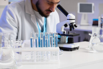 Fototapeta premium Male scientist with microscope and test tubes of water sample working at table in laboratory
