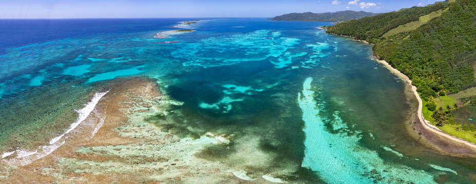 Aerial view of the turquoise coral reefs and lush tropical coastline of Guanaja island under a clear blue sky Guanaja, Bay Islands Department, Honduras.