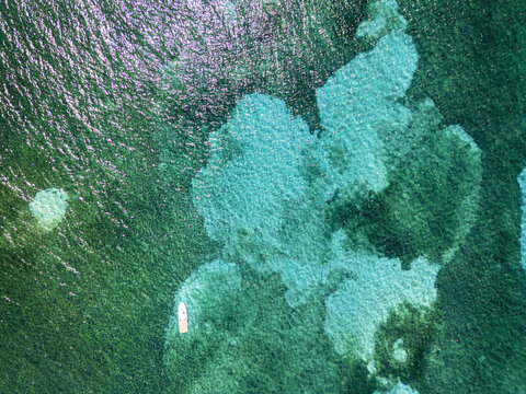 Aerial view of a small white boat floating on crystal clear turquoise water over coral reefs Guanaja, Bay Islands Department, Honduras.