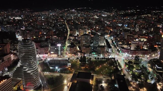 Aerial perspective descending over downtown Tirana, Albania, showcasing illuminated city streets, modern architectural skyscrapers like TID Tower, and sprawling nighttime urban grid