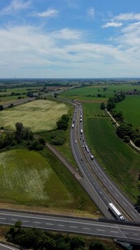 Highway in Rural Landscape: An aerial view of a busy highway winding through a picturesque rural landscape with green fields and distant trees under a clear blue sky.