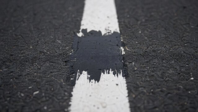 Close-up of a white road line on asphalt, a section painted over with black.