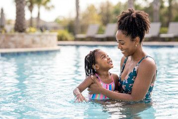 Fototapeta premium African american mother gently teaching her young daughter to swim in a bright outdoor pool