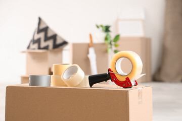 Packing tape dispenser with adhesive rolls and cardboard box in living room on moving day