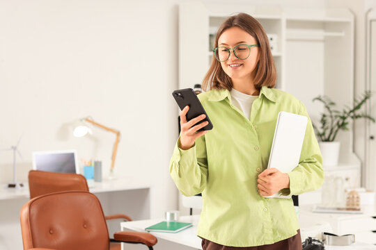 Happy female programmer with laptop and mobile phone working in office