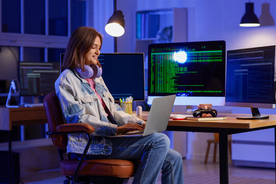 Happy female programmer with headphones, laptop and computers working in office at night