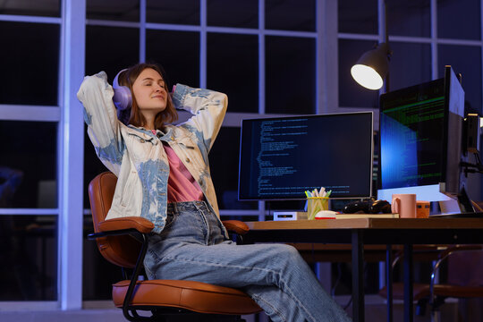 Female programmer with headphones and computers relaxing in office at night