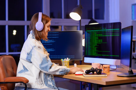 Happy female programmer with headphones and computers working in office at night