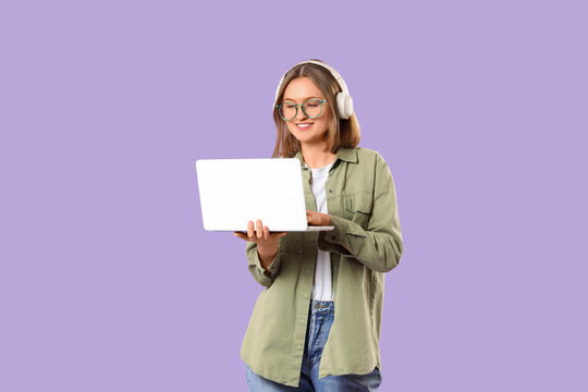 Happy female programmer in headphones working with laptop on purple background