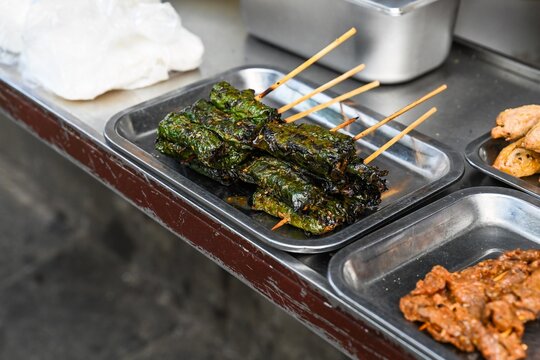Traditional Vietnamese grilled Bo La Lot beef wrapped in lolot leaves on skewers is displayed on a metal tray at a street food stall in Vietnam