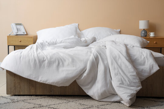 Interior of hotel room with bedside tables, unmade bed and crumpled linen near beige wall