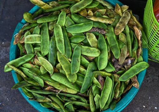 A close up top view of fresh raw green dau ngu lima bean pods displayed inside a plastic container at a traditional street market in Vietnam