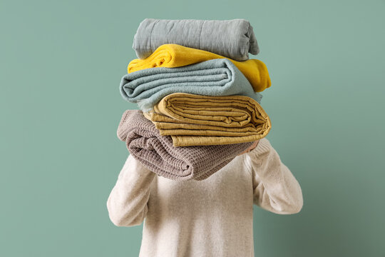 Young woman with stack of different blankets on turquoise background, closeup