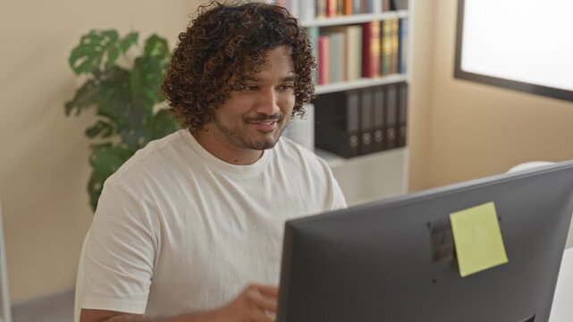 Man at computer in a building leans back with hands behind head and eyes closed, sticky note on monitor, bookshelf and binders nearby; relief break.