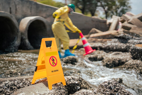 Environmental cleanup worker marking restricted hazardous wastewater area near coastal drainage pipes while conducting pollution inspection and contamination risk assessment outdoors.
