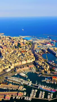 Vertical video. Genoa, Italy. Sweeping Drone footage over the historic Porto Antico and working harbor, dense terracotta rooftops converging on the Ligurian Sea under a clear summer sky. Drone footag