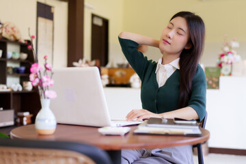 Fototapeta premium Asian businesswoman stretching neck shoulder during remote work break using laptop computer at cafe coffee shop work from anywhere digital nomad lifestyle