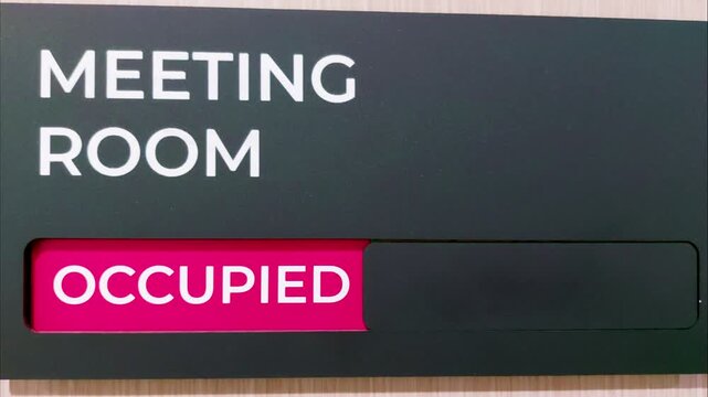 Close up of hand sliding office meeting room door sign from green vacant status to red occupied status, then back again. Concept of workplace privacy, meeting space availability, business organization