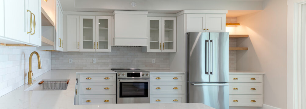 Typical white American kitchen with GFCI outlets along the perimeter, equipped with modern stainless steel appliances, white cabinets, and brass hardware, USA