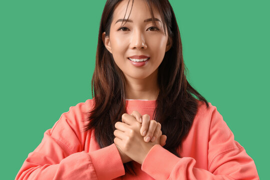 Young happy Asian woman using sign language on green background
