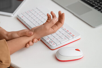 Fototapeta premium Woman suffering from pain in wrist at table in office