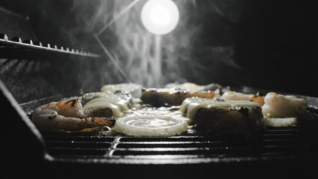 Black and white close up of food grilling on an outdoor barbecue with steam and a bright overhead light