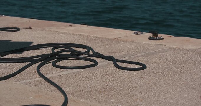 Black mooring rope lying on a marina pier beside seawater.