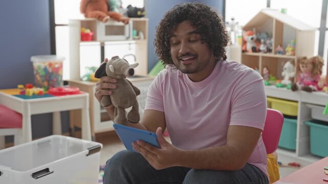 Man holds elephant puppet and tablet, points puppet with hand while smiling and seated in building; playful teaching.