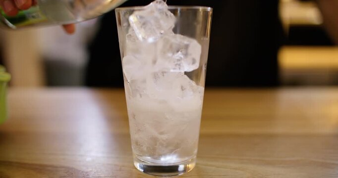 Preparing ice drink. Bartender work. Hand pouring sparkling water from bottle to tall glass with frozen cubes on cafeteria counter.