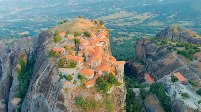 Meteora, Kalabaka, Greece. The Great Meteoron Monastery of the Transfiguration of the Saviour, terracotta rooftops crowning a sandstone pillar, sweeping Drone footage over the Thessaly plain at dawn.