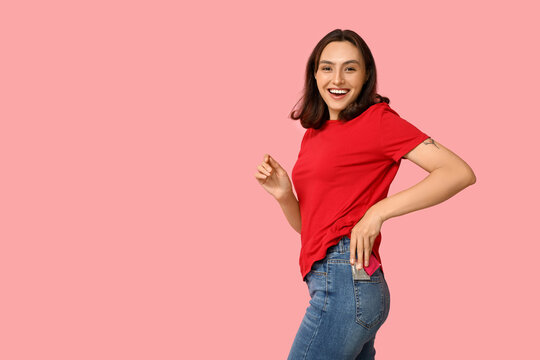 Young woman putting condoms in pocket on pink background. Safe sex concept
