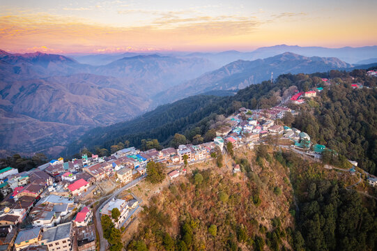 Aerial view of the colorful buildings of Chakrata hill station perched on a mountain ridge during sunset with distant Himalayan peaks in Chakrata, Uttarakhand, India.