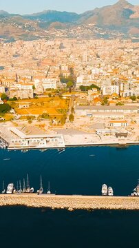 Vertical video. Palermo, Sicily, Italy. Castello a Mare and the port of La Cala, aerial panoramic sweep over the ancient harbor, terracotta rooftops and the Tyrrhenian Sea under clear summer sky. Dro