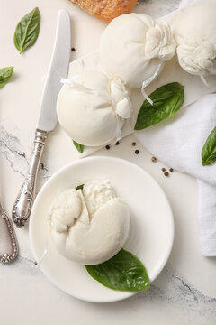 Plate and board of tasty Burrata cheese with basil on white background