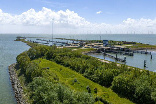 Aerial view of the Lorentzsluizen complex with its locks, lush green vegetation, and distant wind turbines under a cloudy sky in Kornwerderzand, Friesland, Netherlands.