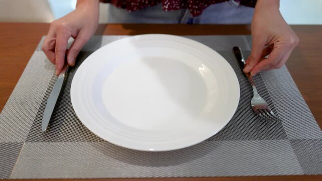 Hands Setting a White Ceramic Plate with Silverware on a Placemat