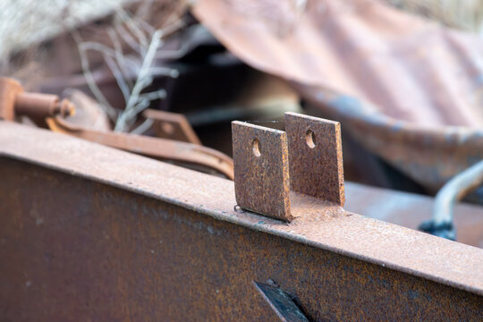 Rusted steel clevis mounting bracket with pinholes welded to a heavy iron beam in an industrial salvage yard close-up.