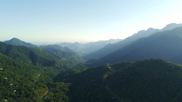 Wide aerial landscape of lush green mountain ranges and a deep valley under a clear blue sky. Scenic view of the Atlantic Forest mountains in Rio de Janeiro state, showing the vast natural landscape a