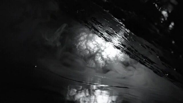 Abstract grayscale scene of water surface reflecting swirling vapor and radiant light creating textured visual effect