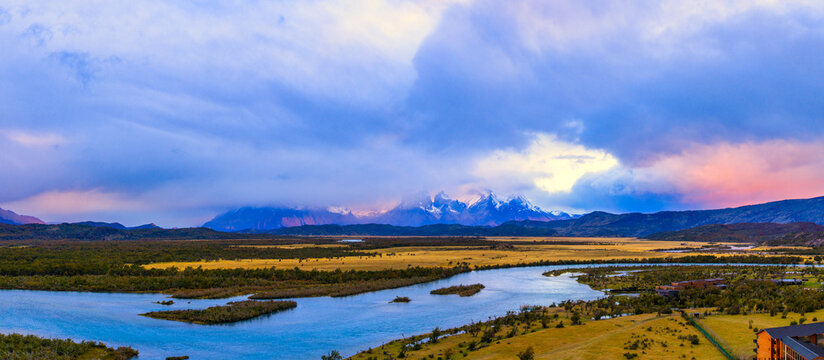Aerial view of Rio Serrano Hotel and Spa by the winding Serrano River with the snow-capped peaks of Torres del Paine under a dramatic sunset sky Torres de Paine, Magallanes, Chile.