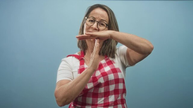 Woman wearing red check apron makes a t hand gesture while water drips between her palms in studio; household patience.
