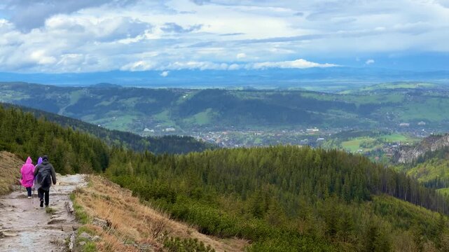 Family in rain ponchos hiking along mountain ridge in Tatra Mountains near Zakopane, Poland. Slow motion outdoor travel footage with panoramic landscape, trekking and adventure lifestyle.