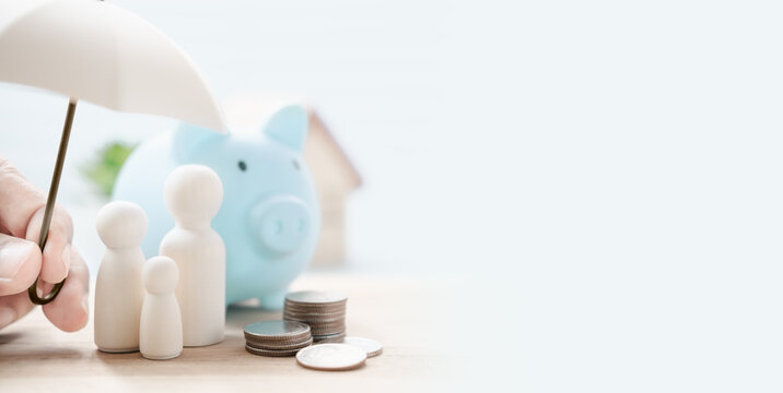 Family Financial Protection Concept with Wooden Figures Under Umbrella Beside Piggy Bank Coins and House Symbol in Soft Blue Background Representing Insurance Savings Security and Future Planning